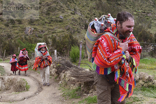 Tourist in traditionellem Poncho der Quechua Indios hilft Einheimischen beim Tragen des Wocheneinkaufs  Anden  bei Machu Picchu  Cusco  Peru  Südamerika