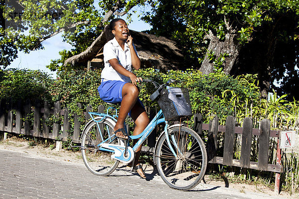 Frau telefoniert beim Fahrradfahren mit dem Handy  Insel La Digue  Seychellen  Afrika  Indischer Ozean