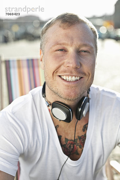 Porträt eines glücklichen Mannes mit Kopfhörern am Strand