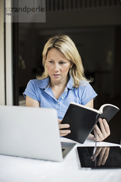 Mittlere erwachsene Frau mit Laptop und digitalem Tablet-Haltebuch