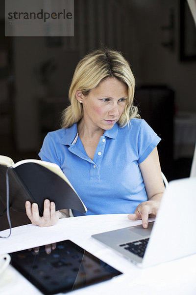 Mittlere erwachsene Frau mit Buch und digitalem Tablett mit Laptop