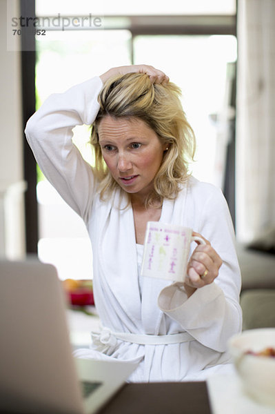 Verzweifelte Frau mit Kaffeetasse bei der Arbeit am Laptop zu Hause