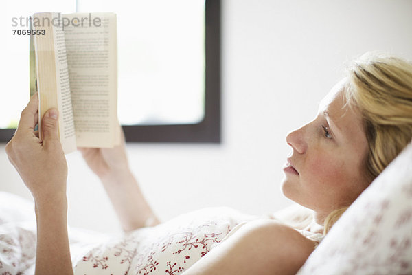 Seriöse erwachsene Frau auf dem Bett liegend und Lesebuch