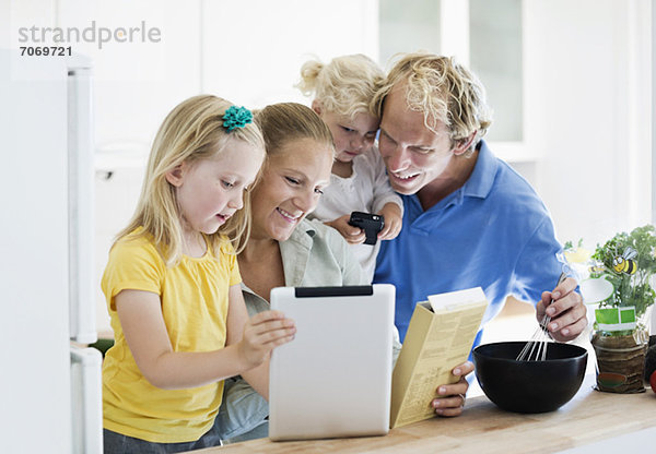 Kleines Mädchen mit Eltern mit digitalem Tablett für das Rezept in der Küche