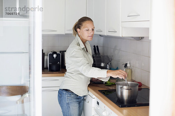 Mittlere erwachsene Frau bei der Zubereitung von Speisen in der Küche