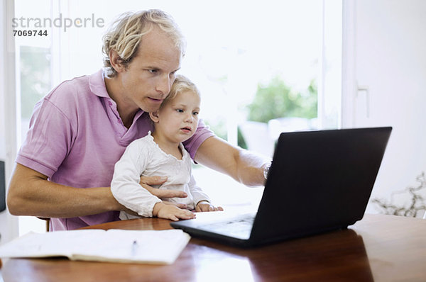 Mittlerer erwachsener Mann mit Laptop und Tochter am Schreibtisch