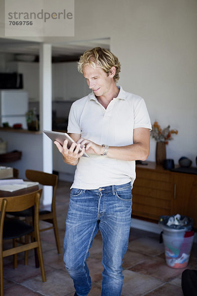 Mittlerer Erwachsener Mann  der zu Hause ein digitales Tablett benutzt.