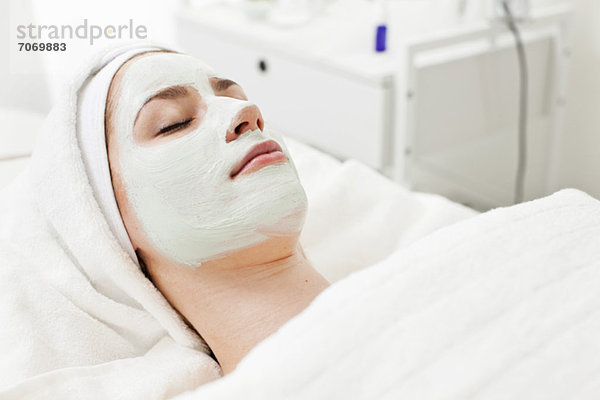 Junge Frau entspannt auf Massagetisch mit Gesichtsmaske im Beauty Spa