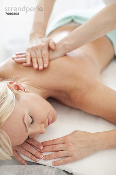 Mittlere erwachsene Frau entspannt mit geschlossenen Augen und Masseurin bei einer Massage