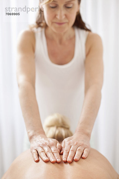 Reife Masseurin massiert den Rücken einer erwachsenen Frau im Wellnessbereich.