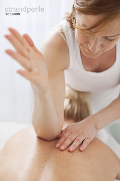 Reife Therapeutin  die den Rücken einer erwachsenen Frau mit Ellenbogen massiert.
