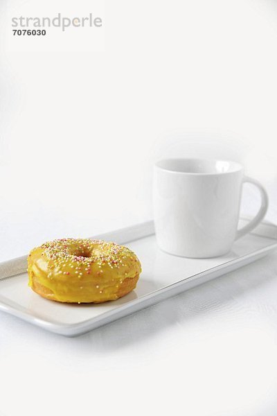 Doughnut mit gelber Glasur und Zuckerperlen und eine Tasse