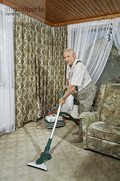Älterer Mann beim Hausputz mit Staubsauger