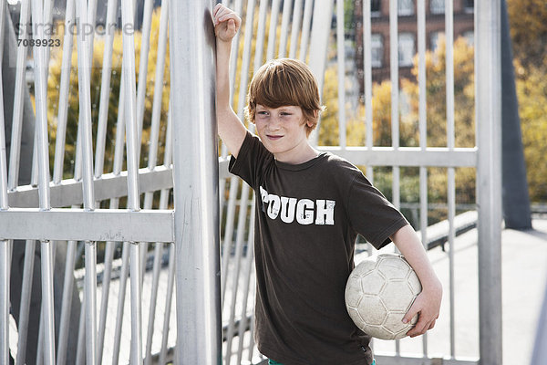 Junge steht mit Fußball auf einem Sportplatz