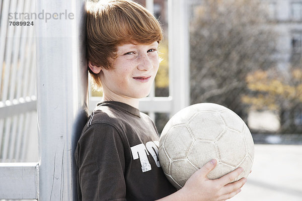 Junge steht mit Fußball auf einem Sportplatz