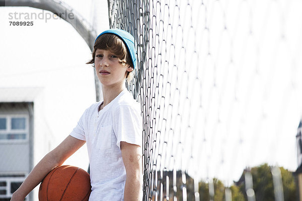 Junge steht mit Basketball an einem Zaun