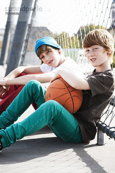 Zwei Jungen sitzen mit Basketball an einem Zaun