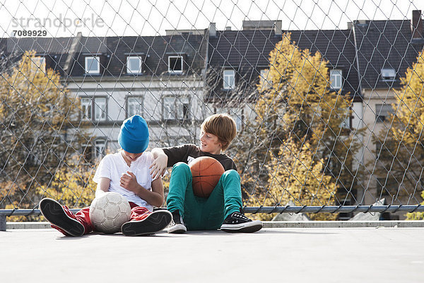 Zwei Jungen sitzen auf einem Sportplatz mit Bällen