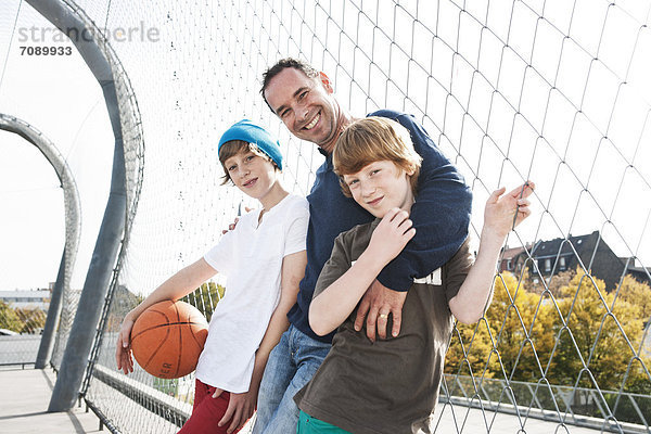 Vater und zwei Söhne mit Basketball auf einem Sportplatz