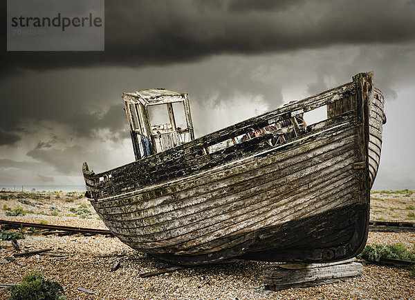 A wooden fishing boat  on the beach at Dungeness. A dark stormy sky.