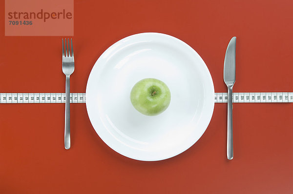 Green apple on plate with fork  knife and measuring tape