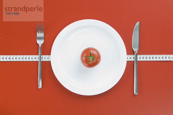 Red tomato on plate with fork  knife and measuring tape