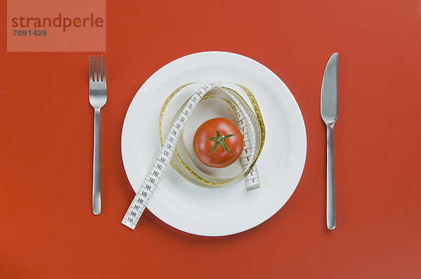Rote Tomate auf Teller mit Gabel  Messer und Maßband