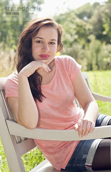 Young woman sitting on park bench  smiling  portrait