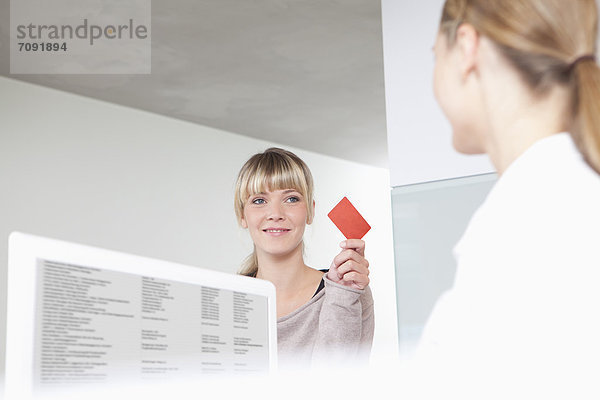 Germany  Patient giving insurance card to receptionist in dental office