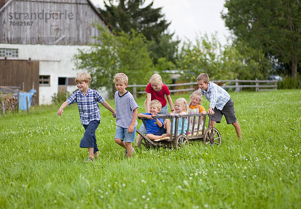Germany  Bavaria  Group of children playing with hand cart in front of farmhouse