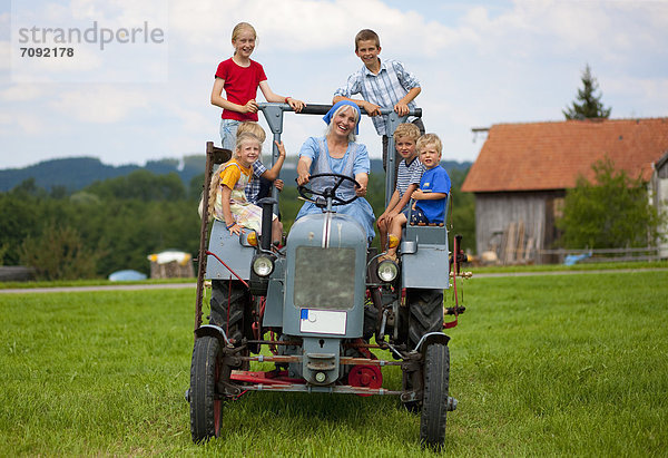 Woman with group of children sitting on old tractor in front of farmhouse