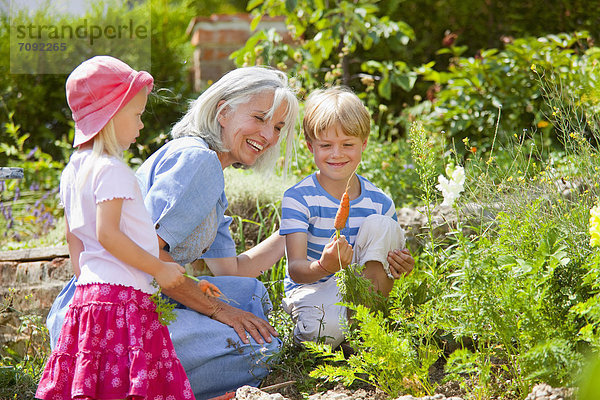 Germany  Bavaria  Grandmother with children inspecting carrots in garden