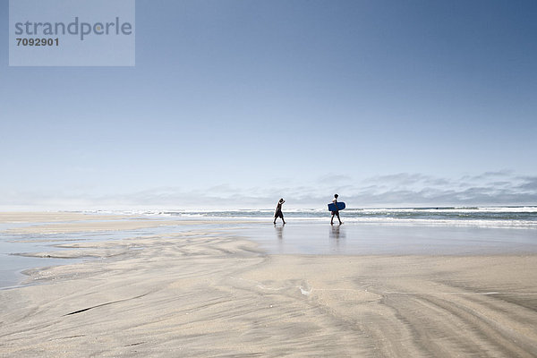 France  Two boys walking on beach with body surfboards