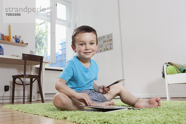 Junge sitzend auf dem Boden mit Buch  lächelnd  Portrait
