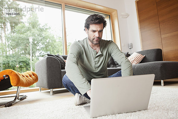 Erwachsener Mann mit Laptop im Wohnzimmer