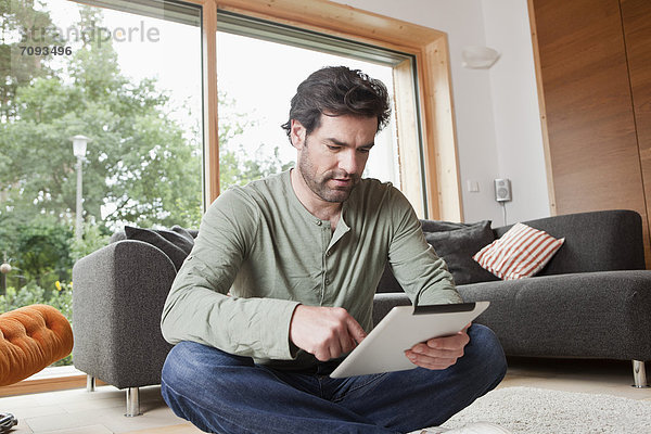 Erwachsener Mann mit digitalem Tablett im Wohnzimmer