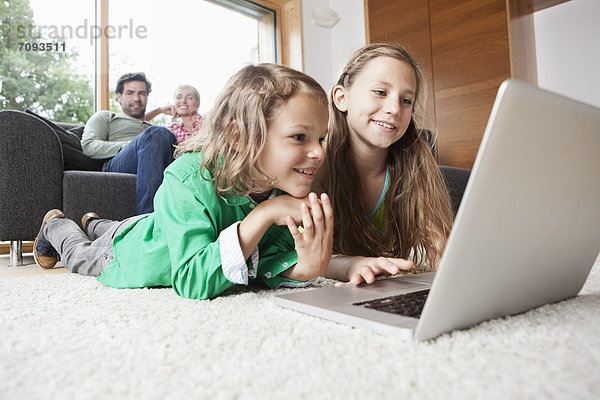 Mädchen und Junge mit Laptop im Wohnzimmer