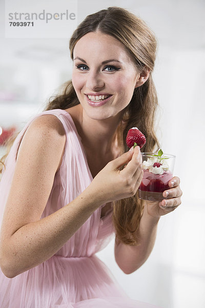 Germany  Young woman holding strawberry in her hand  smiling  portrait