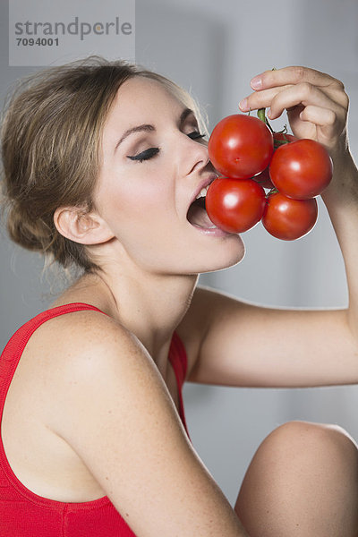 Germany  Young woman biting tomatoes  close up