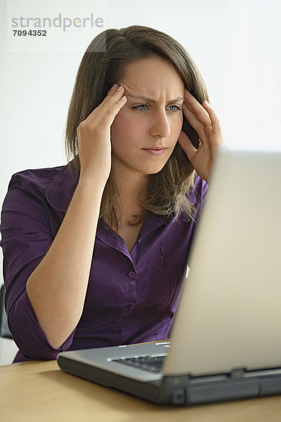 Junge Frau mit Kopfschmerzen bei der Arbeit am Laptop