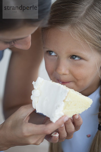 Mutter füttert ein Stück Kuchen an ein kleines Mädchen.