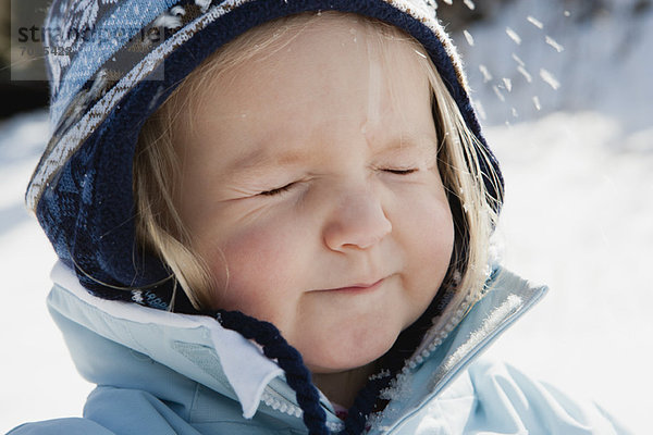Kleinkind Mädchen in Winterkleidung im Schnee mit geschlossenen Augen  Portrait