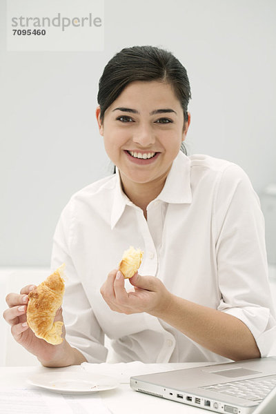 Junge Frau isst Croissant  lächelnd