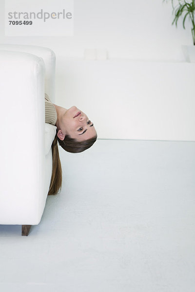 Junge Frau auf Sofa liegend mit baumelndem Kopf  Tagträumen