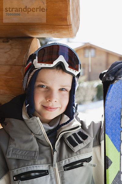 Junge mit Skibrille und Skijacke und hält Snowboard  Portrait