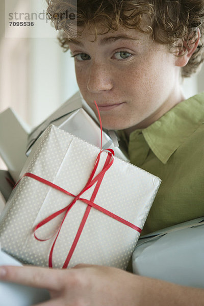 Ein Junge  der einen Haufen Geschenke hält.