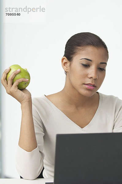 Junge Frau beim Apfelessen am Schreibtisch
