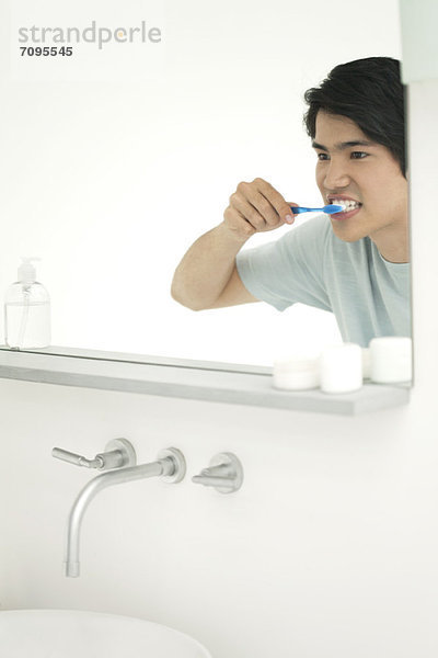 Junger Mann schaut in den Spiegel  putzt die Zähne