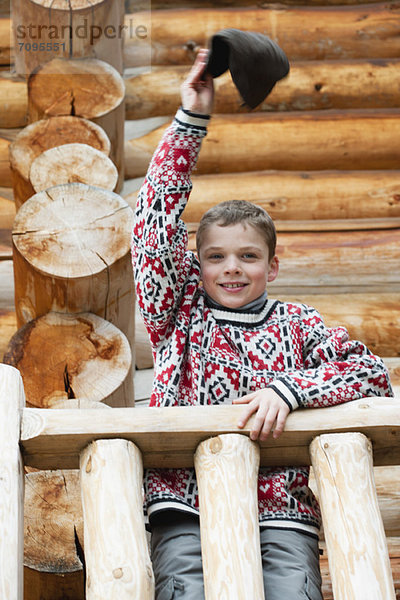 Junge steht auf Deck der Blockhütte  winkender Hut vor der Kamera  Porträt