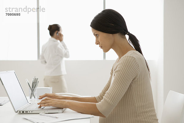 Junge schwangere Frau beim Tippen am Laptop im Büro  hintergrundbeleuchtet